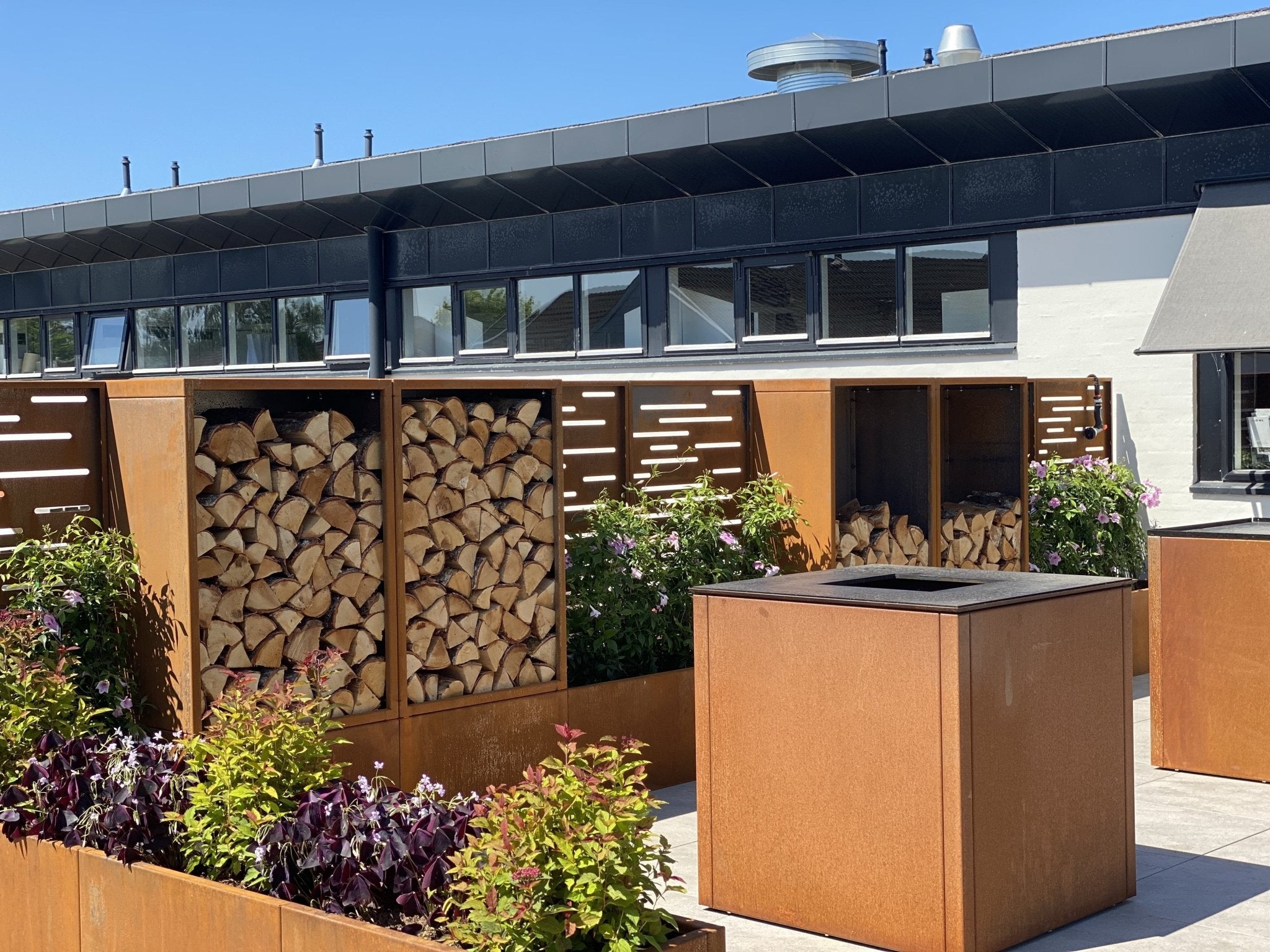 byJEMA Feuerstelle aus Cortenstahl mit Grillrost und integrierter Holzlagerung – Outdoor-Feuerlösung im modernen Gartendesignhavemiljø