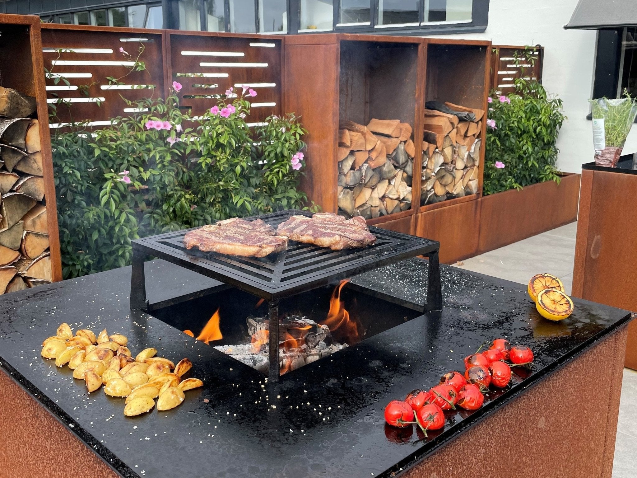 byJEMA Feuerstelle aus Cortenstahl mit Grillrost – Steaks und Gemüse werden über offenem Feuer im Garten zubereitet