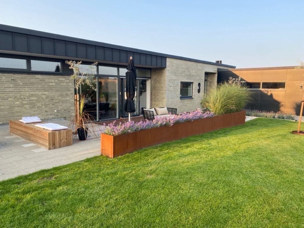 Langer Pflanzkasten aus Cortenstahl von CUBY mit Blumen und Gräsern am Haus