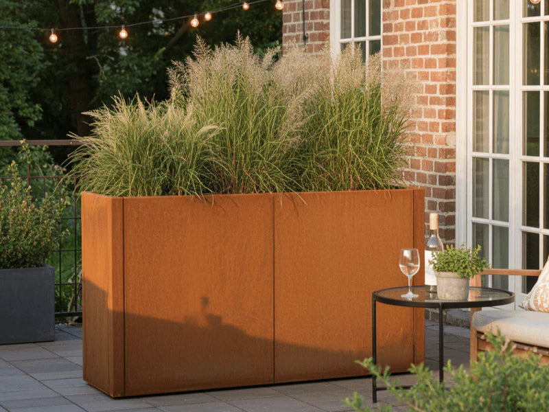 CUBY Pflanzkasten aus Cortenstahl mit hohem Ziergras auf Terrasse bei Backsteinhaus