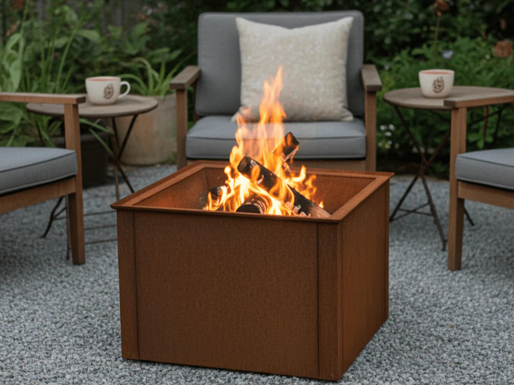 Quadratische Feuerschale aus Cortenstahl mit brennendem Holzfeuer in moderner Gartensitzgruppe
