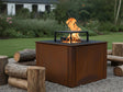 CUBY Feuergrill aus Cortenstahl mit sichtbaren Flammen im grünen Naturgarten