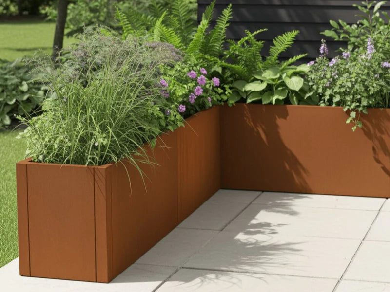 L-förmiger Pflanzkasten aus Cortenstahl von CUBY mit Blumen und Gräsern im Garten