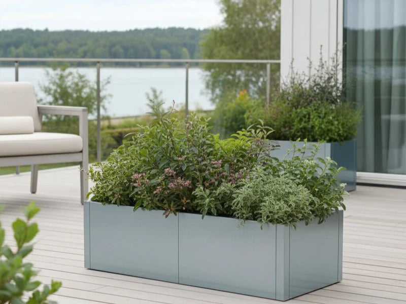 CUBY niedriger Pflanzkübel aus verzinktem Stahl mit grünen Pflanzen auf Terrasse mit Ausblick