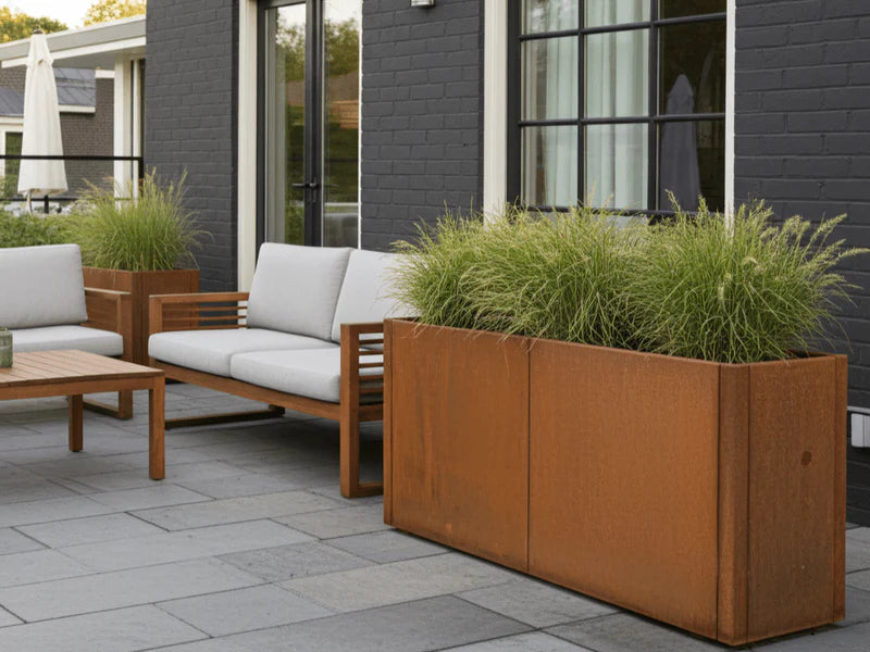 Rechteckiger CUBY Pflanzkasten aus Cortenstahl mit Ziergräsern vor modernem Haus